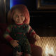 Chucky, killer doll, sits in front of a cozy fire